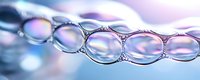 Macro photography of soap bubbles forming chain pattern with iridescent rainbow colors and reflections on blurred purple and blue background.