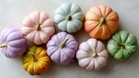 Colorful decorative pumpkins in pastel pink, purple, mint green, and orange shades arranged on light background. Seasonal autumn harvest composition.