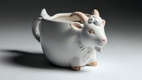 Adorable white ceramic cow-shaped mug with horns and udder details on neutral background for kitchen decor and novelty drinkware concepts.