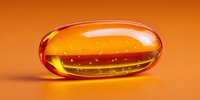 Glossy orange vitamin capsule with golden oil inside on warm orange background for health and wellness supplement advertising.
