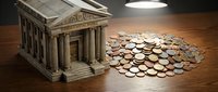 Miniature bank building with scattered coins on wooden surface under warm lighting representing financial savings and investment concepts.