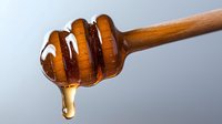 Wooden honey dipper with golden honey dripping, natural sweetener for cooking, baking and healthy eating on neutral background.