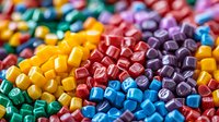 Colorful plastic letter beads in vibrant rainbow colors create abstract educational background pattern, macro photography shows texture and shine for craft projects.