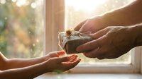 Hands exchanging wrapped gift box by sunny window, giving present gesture between two people, holiday celebration and generosity concept for greeting cards.