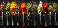 Aromatic spices and herbs in vintage silver spoons on dark background, colorful seasoning mix with peppercorns arranged in line, culinary concept.