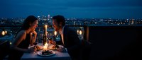 Romantic couple enjoying candlelit dinner on rooftop terrace with city skyline at night, intimate dining experience for anniversary celebration.
