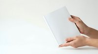 Person with medium skin tone holding blank white paper or document against neutral background, suitable for business, education, and marketing materials.