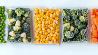 Frozen vegetables in transparent plastic bags arranged in row showing peas, broccoli, corn, mixed vegetables and carrots for healthy meal preparation.