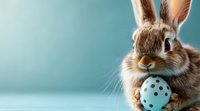 Adorable brown bunny with long ears holding blue polka dot Easter egg against turquoise background, close-up portrait with copy space for holiday designs.