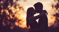 Romantic couple silhouette kissing at golden sunset with warm bokeh lights creating intimate atmosphere for love and relationship concepts.