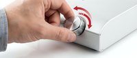 Hand adjusting volume control knob on white audio device with red indicator markings for sound level management and equipment operation.
