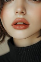 Close-up portrait of Asian woman's face focusing on coral matte lipstick, pale complexion, and natural makeup look against dark background. For beauty and cosmetic advertising.