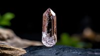 Clear quartz crystal point with natural inclusions and termination on dark stone surface with blurred natural background for healing and meditation practices.