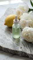 Green facial serum in dropper bottle with fresh lemon and white peonies on concrete surface for skincare, beauty and cosmetic product marketing.
