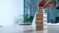Professional businessman hand placing wooden block with lightbulb icon on tower stack in modern office environment for business strategy concepts.