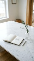 Open notebook with hello lettering on marble table, eucalyptus sprig in glass vase, minimalist home workspace, natural light interior.