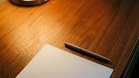 Blank white paper with pen on wooden desk surface, suitable for writing, planning, business correspondence, and creative projects.