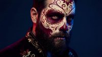 Bearded man with ornate skull face paint in traditional Day of the Dead style against dark background for Halloween and cultural celebration designs.