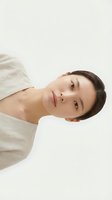 Young woman with dark hair and fair complexion wearing light beige t-shirt, tilting head against white background. Suitable for beauty, wellness, skincare and lifestyle marketing campaigns.