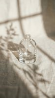 Empty glass bottle with rounded shoulders on neutral linen fabric, sunlight casting geometric window shadows, minimalist composition for cosmetics, perfume, or skincare product packaging mockups.