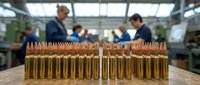 Rows of golden ammunition bullets lined up on wooden surface with blurred workers in industrial manufacturing facility background for military defense concepts.