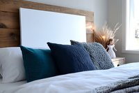 Cozy bedroom interior with white bedding and textured navy blue and teal decorative pillows against wooden headboard, dried pampas grass decor on nightstand.