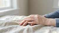 Elderly hands resting gently on a linen surface near a window, conveying care, comfort, and support in a soft, natural light setting.