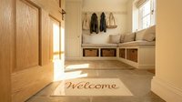 Bright and cozy home entryway with a welcome mat, built-in bench, wicker baskets, and coat hooks in warm neutral tones.