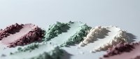 Colorful crushed eyeshadow powder makeup cosmetics in pink green and white shades scattered on clean surface for beauty and fashion applications.