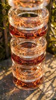 Stack of crystal whiskey glasses with amber liquid reflecting warm golden sunlight creating artistic light patterns and shadows on textured surface.