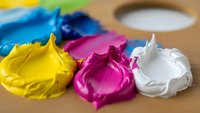 Vibrant acrylic paint dollops in yellow, magenta and white on wooden palette. Art supplies for creative projects, painting techniques and color mixing.