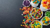 Colorful assorted candies and sweets in white bowls on dark slate background. Variety of rainbow gumballs, cereal rings and confectionery treats for party.