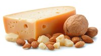 Large piece of yellow cheese with holes next to whole and chopped almonds and walnuts on white background, isolated dairy and nuts composition for food design.