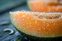 Fresh juicy cantaloupe melon slice with water droplets on rustic wooden surface, showcasing vibrant orange flesh and green rind for food photography.
