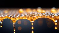Glowing honey drops forming on honeycomb edge with dramatic lighting and bokeh effect against dark background, macro photography showing natural crystallization process.