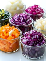 Fresh chopped vegetables in glass bowls including purple cabbage, carrots, cucumber and onion. Colorful ingredients ready for salad or cooking preparation.