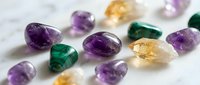 Collection of polished gemstones including amethyst, citrine and malachite crystals scattered on white marble surface for jewelry making and healing.
