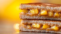 Grilled sandwich with melted cheese and sweet corn kernels on toasted bread, macro shot with warm golden bokeh background showing delicious comfort food.