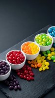 Colorful rainbow jelly beans arranged in white bowls on dark slate surface creating vibrant candy display for celebrations and sweet treats.