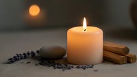 Burning candle with lavender sprigs, cinnamon sticks and smooth stone creating peaceful spa atmosphere for relaxation and aromatherapy sessions.