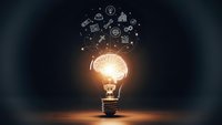 Glowing light bulb with floating business icons representing innovation, creativity and entrepreneurship concepts for marketing and startup projects.