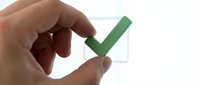 Hand holding green checkmark over checkbox completing task or survey with fingers pinching approval symbol for business success and quality control.