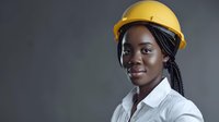 Young African American female construction engineer or architect wearing yellow hard hat and white shirt smiling confidently against dark background.
