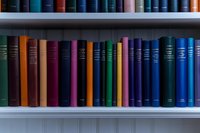 Colorful hardcover books arranged on white library shelves, showing spines in various shades of blue, green, red, and purple, creating academic atmosphere.