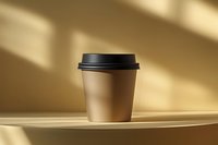 Disposable brown paper coffee cup with black lid on beige surface under dramatic window light and shadows creating minimalist composition.