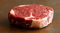 Fresh raw ribeye steak with marbling on dark wooden background, close up view of premium beef cut showing texture and fat distribution for cooking.