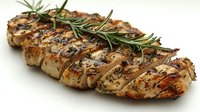 Grilled chicken breast with rosemary herb garnish, diagonal cuts showing juicy meat texture, seasoned with herbs and spices on white background.