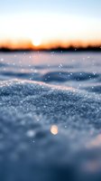 Sparkling snow crystals catch golden sunset light creating magical winter atmosphere with blurred horizon and glowing sky, macro close-up view of frozen landscape.