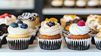Assorted gourmet cupcakes topped with swirled buttercream frosting and fresh berries in chocolate paper cups, arranged in bakery display for dessert menu.