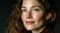 Natural portrait of confident middle-aged Caucasian woman with wavy brown hair and freckles against dark background for lifestyle and beauty content.